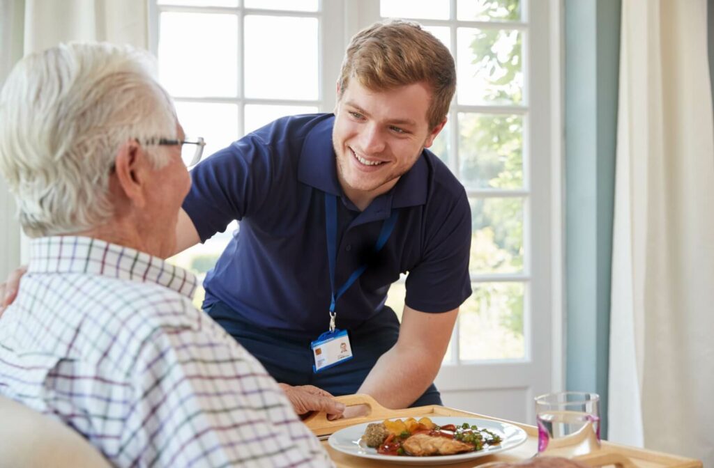 An assisted living staff serving food to an older adult resident.