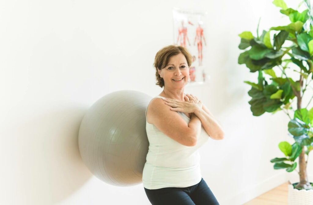 An older adult woman doing wall squats with the aid of an exercise ball.