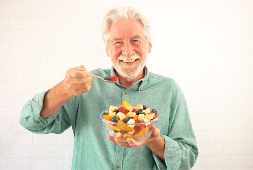 A smiling senior man holding a bowl of fruit salad.