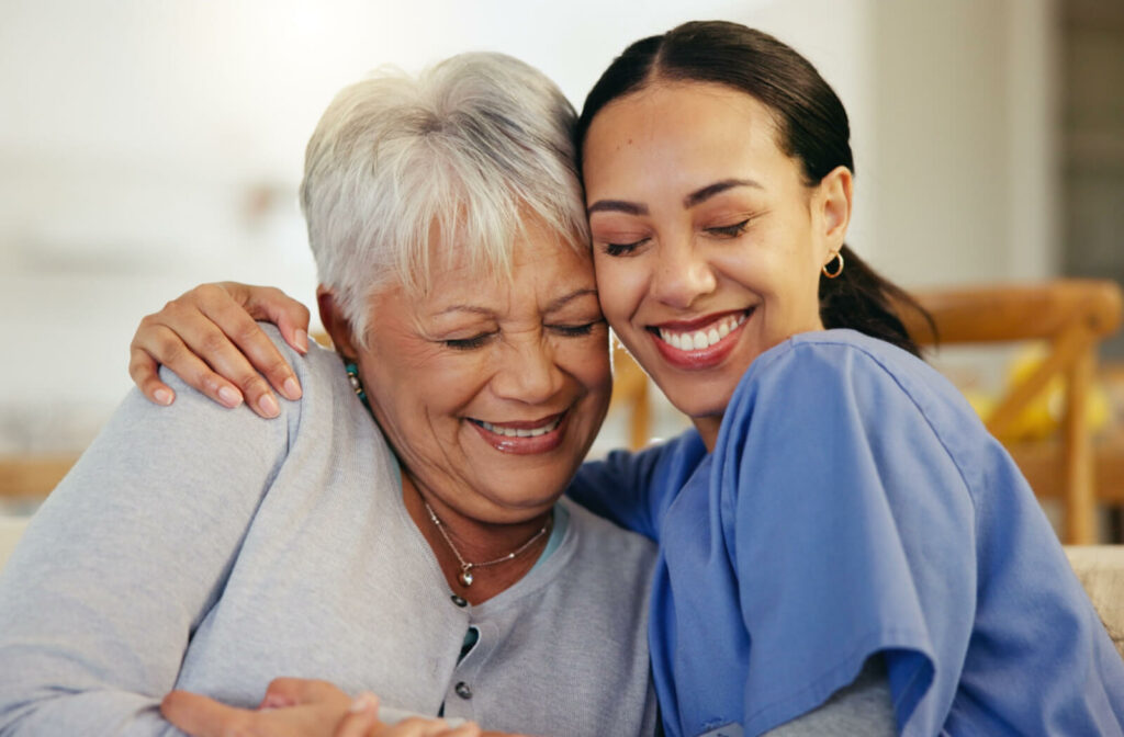 An older adult with dementia staring out the window in frustration while their adult child rests a hand on their shoulder to support them.