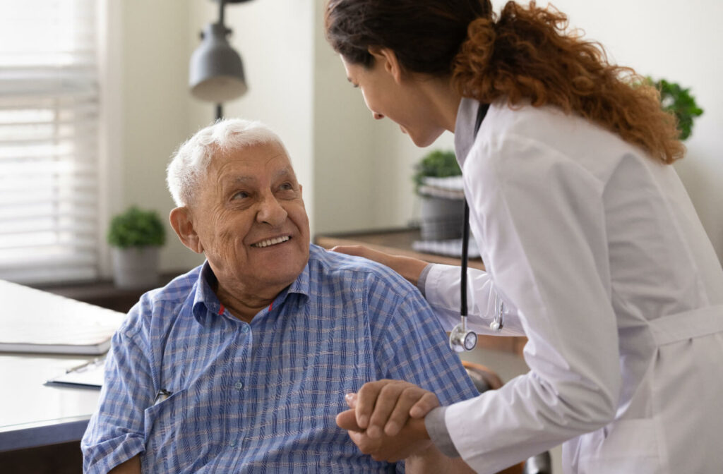 A professional caregiver smiling and helping an older adult stand after a routine checkup in senior living.